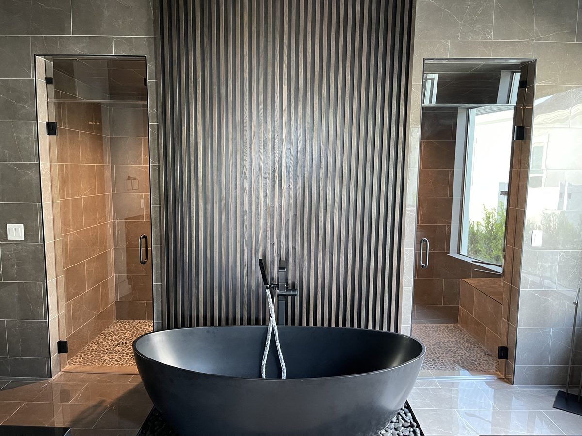 Spa bathroom with sculptural black tub, fluted feature wall, and dual glass showers